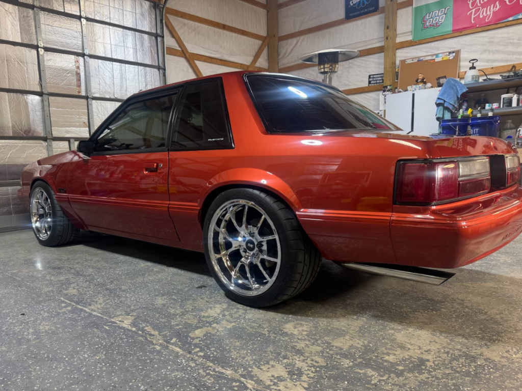 A red Mustang car, vintage from the early 1990s with chrome wheels and a new showroom finish sitting in a garage. | Mystic AC Detailing