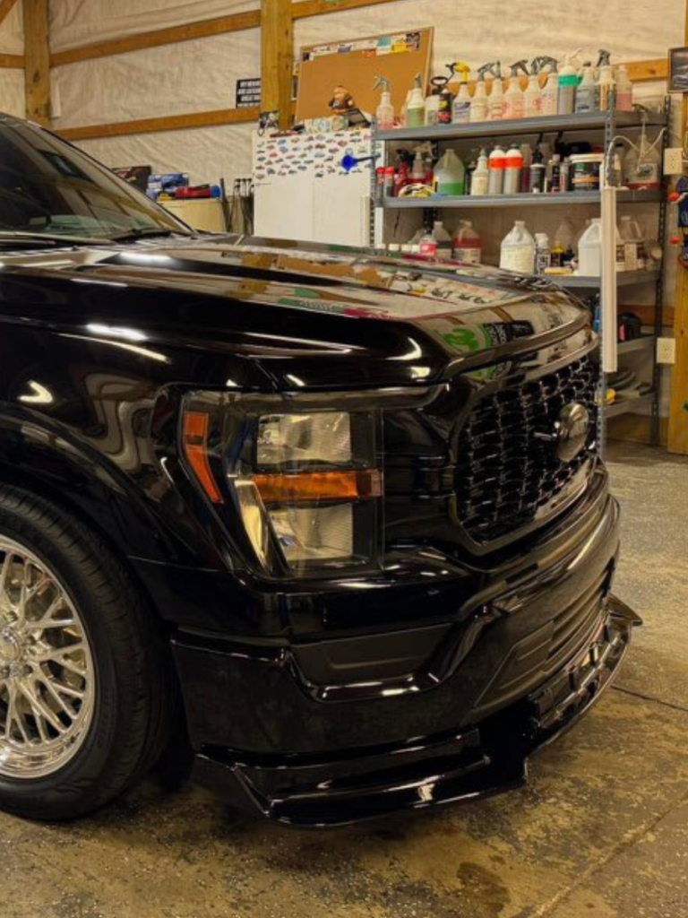 The front of a black FORD Truck that has been detailed and polished sitting in a garage.